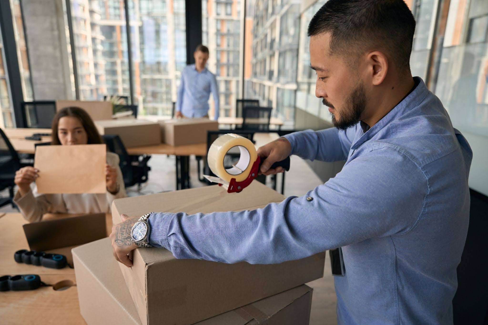 employee sealing a cardboard box with a tape dispenser