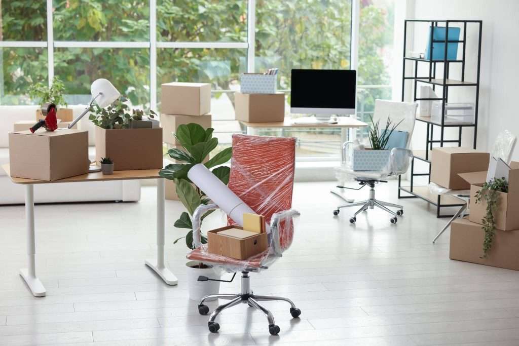 office workspace with packed boxes, wrapped chairs, and equipment prepared for a business relocation.